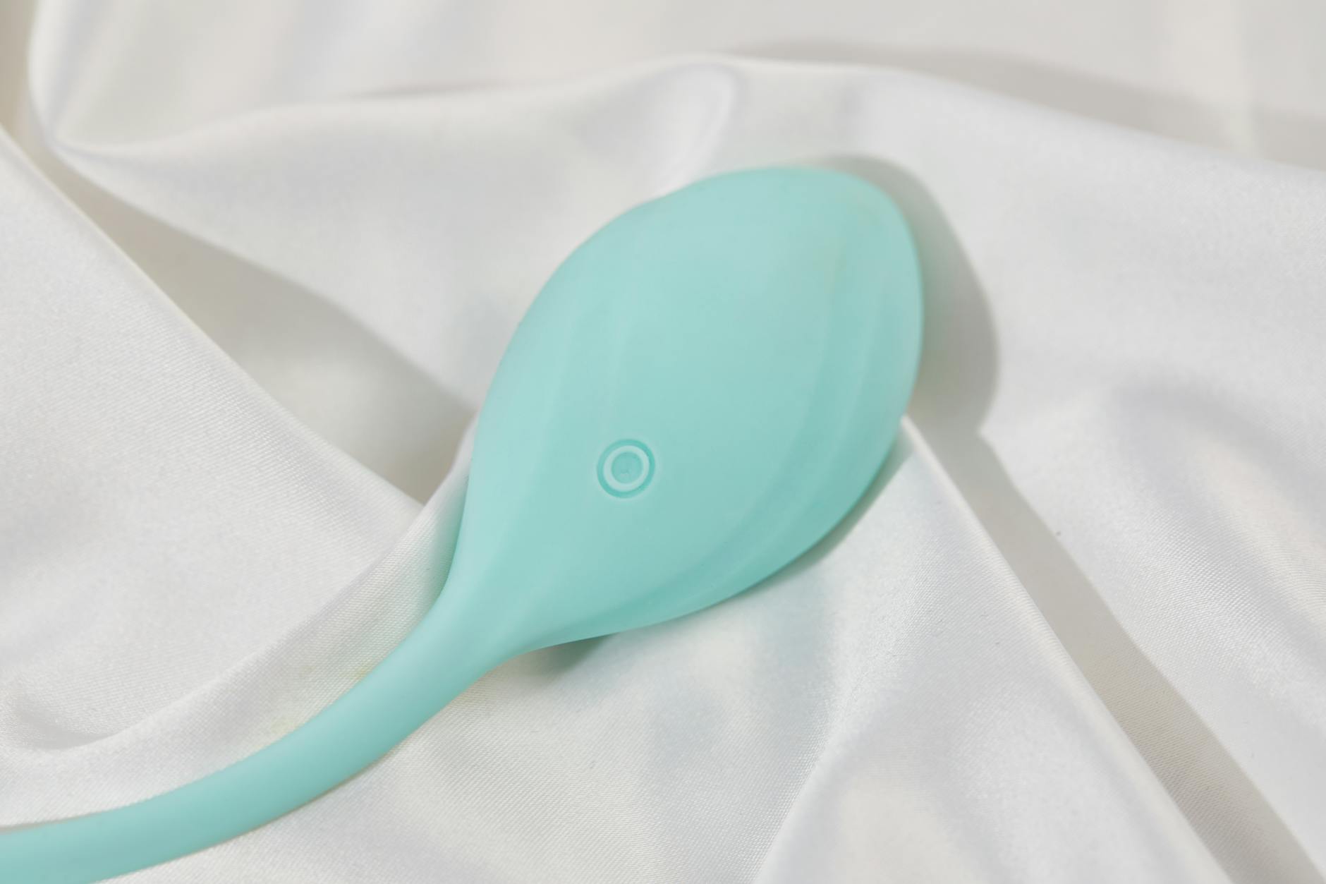 A stylish vibrator on smooth white silk fabric, representing intentional pleasure and self-exploration.