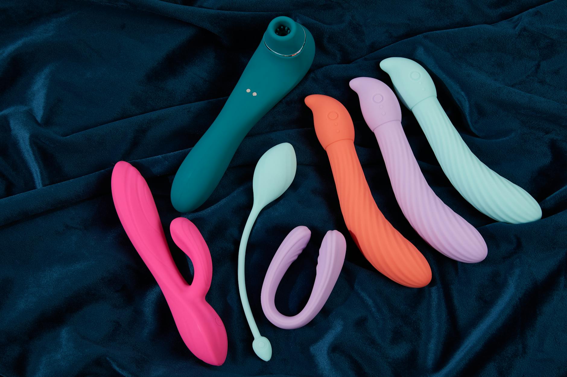 Colorful clitoral vibrators on dark fabric showcasing various shapes and designs
