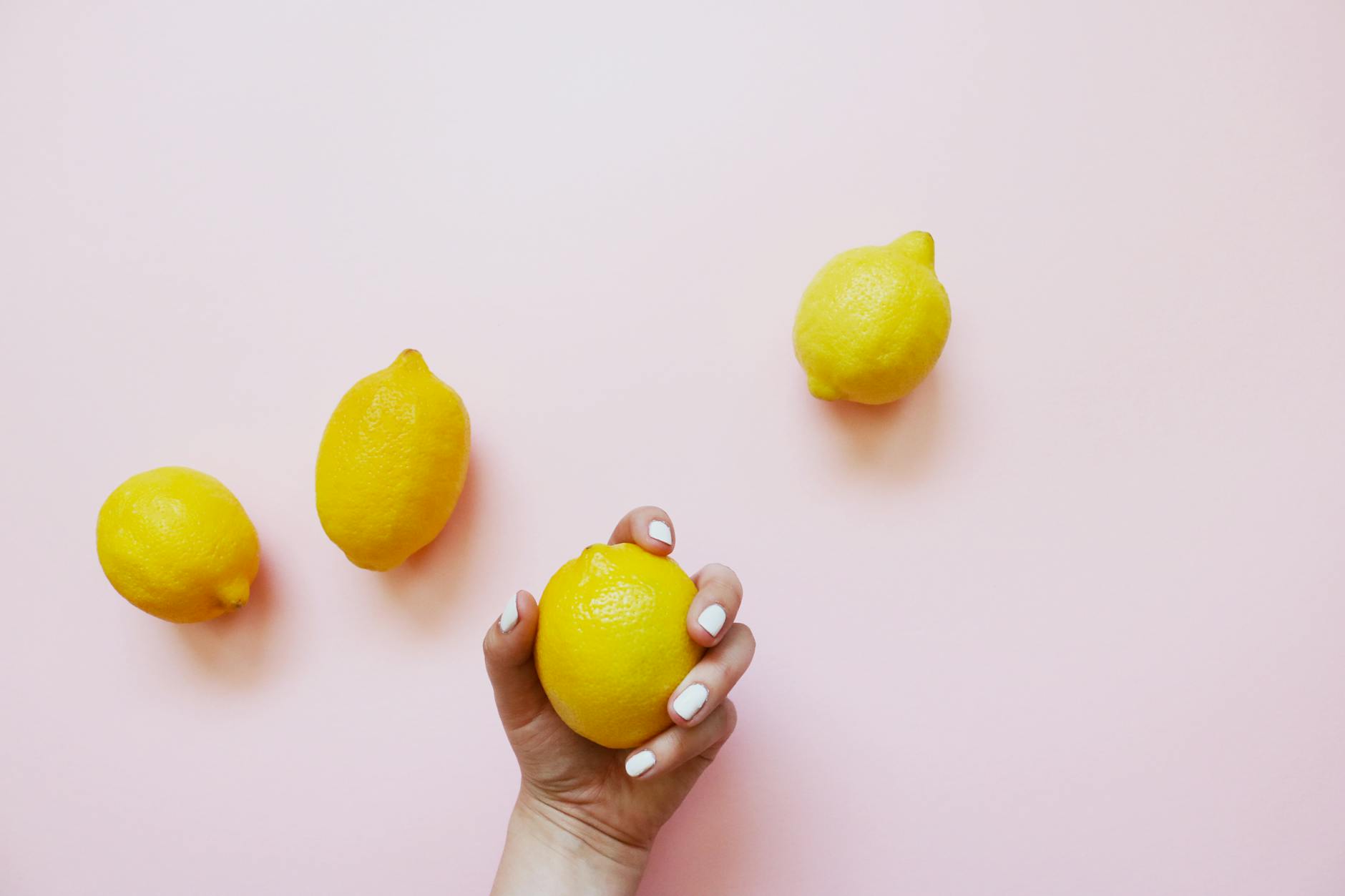 A hand holding a fresh lemon against a soft pink background, symbolizing refreshment and renewal.
