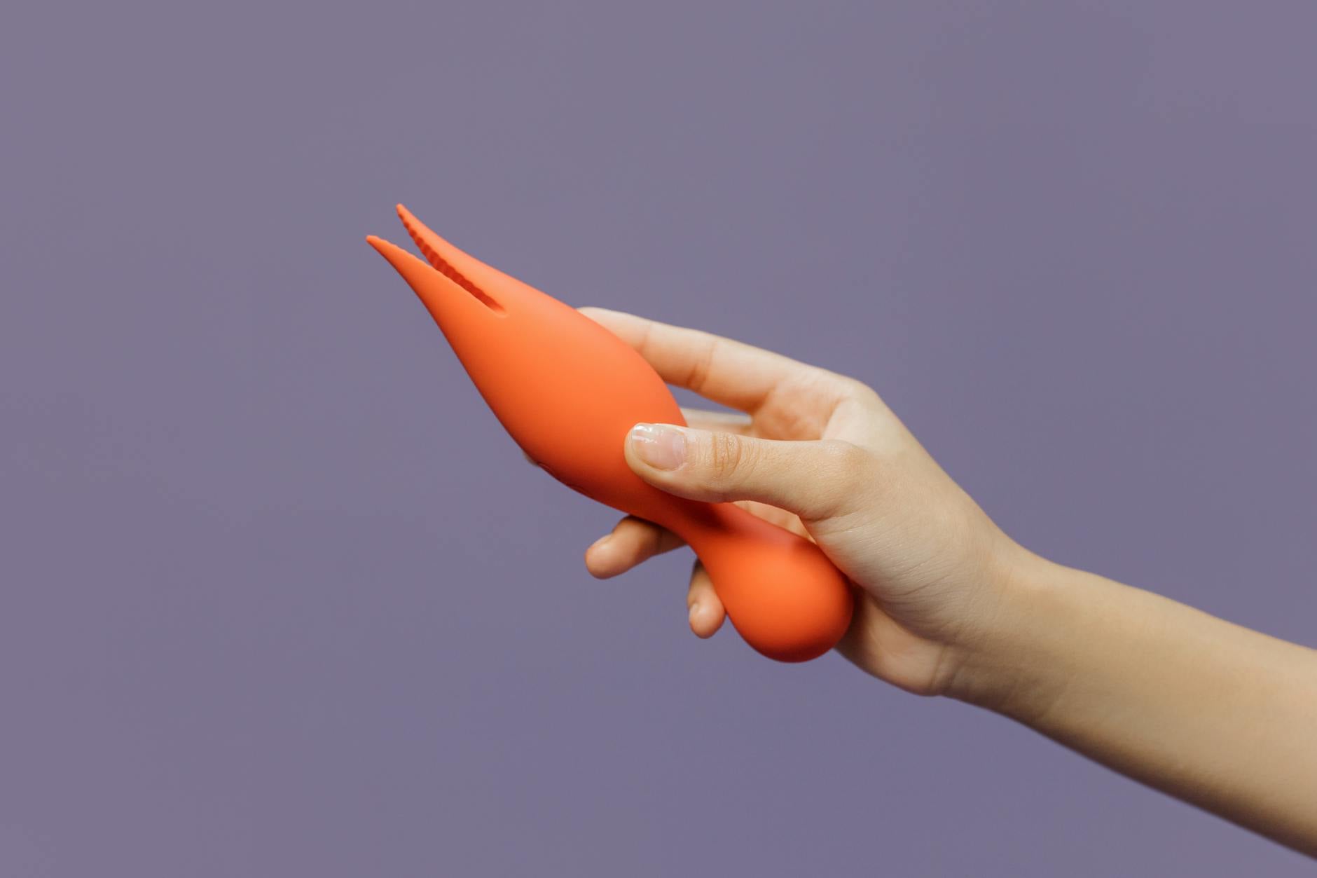A hand holding a lemon vibrator against a minimalistic purple backdrop, representing intimacy and connection.