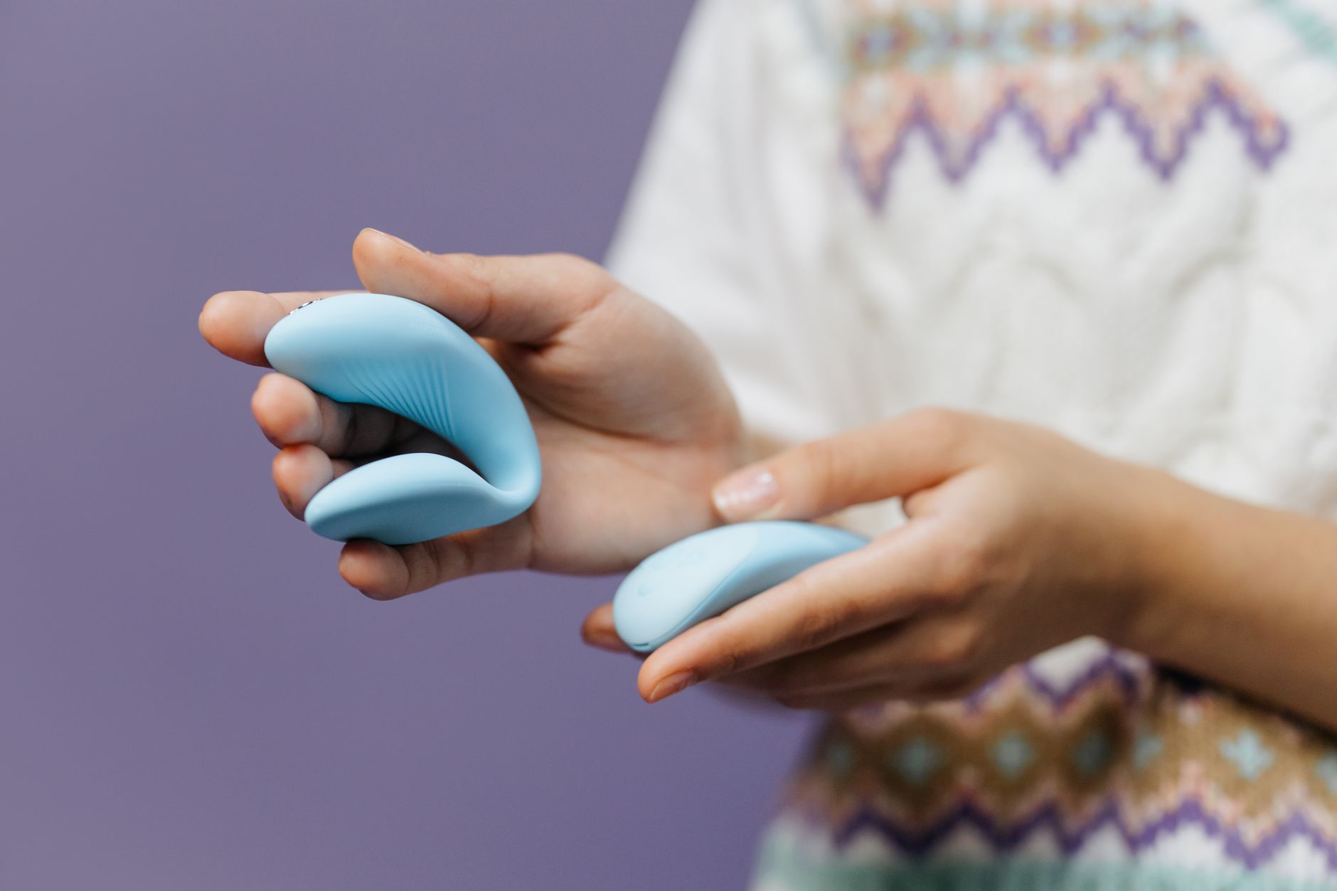 Hand holding a sleek clitoral vibrator against a purple background
