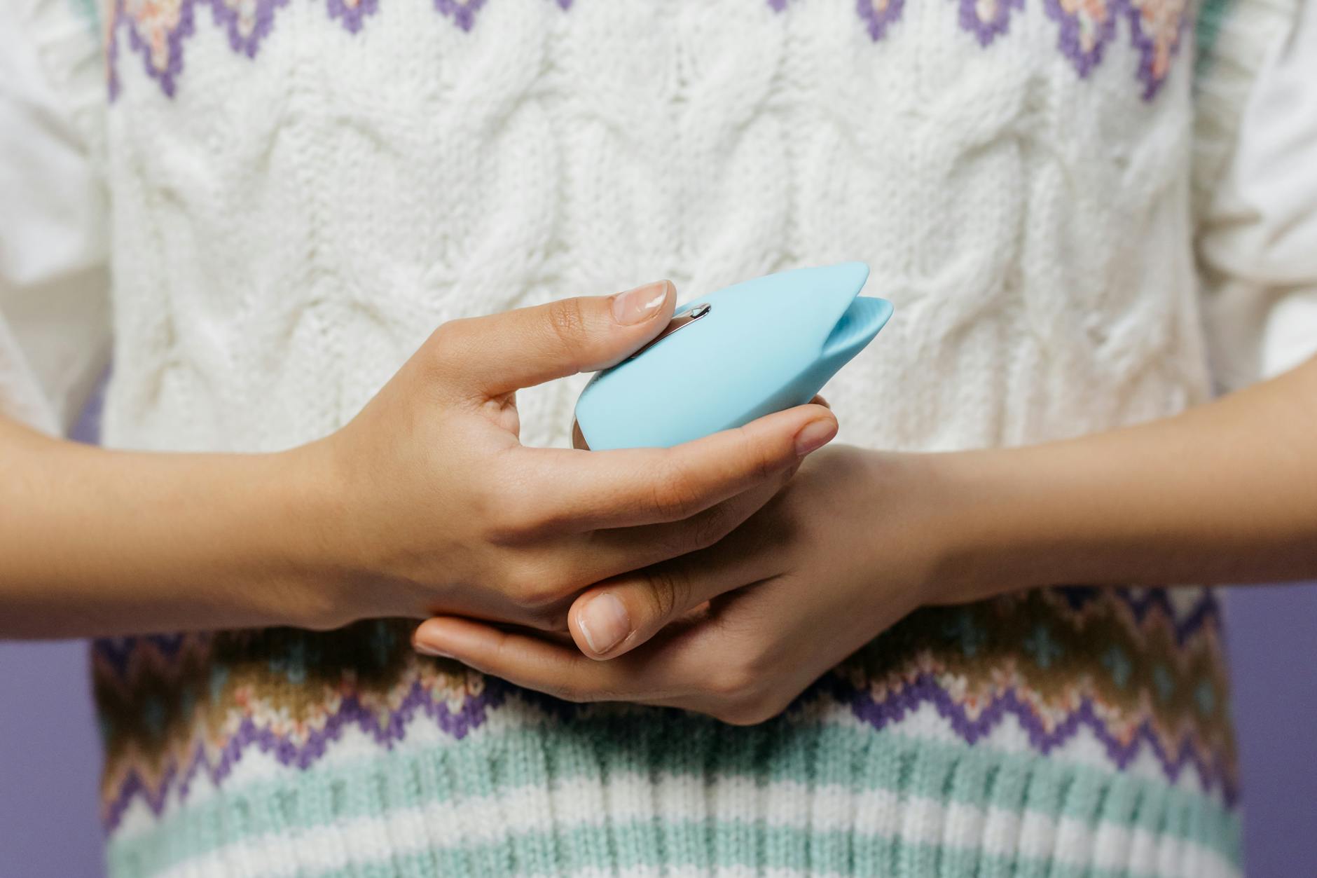 Mão segurando um vibrador pessoal azul contra uma malha de suéter