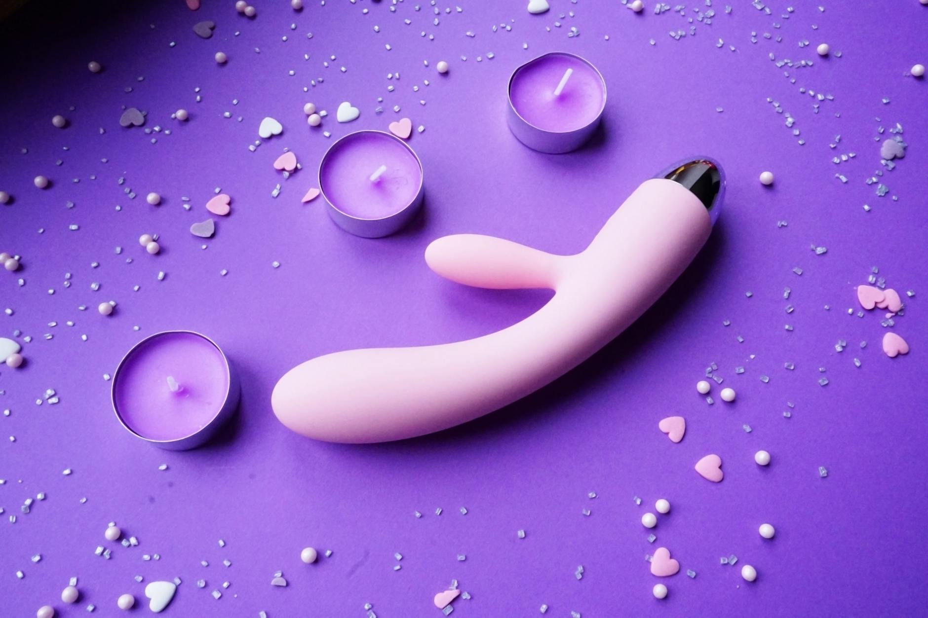 Pink lemon clitoral vibrator on purple background with heart confetti and candles for romantic ambiance