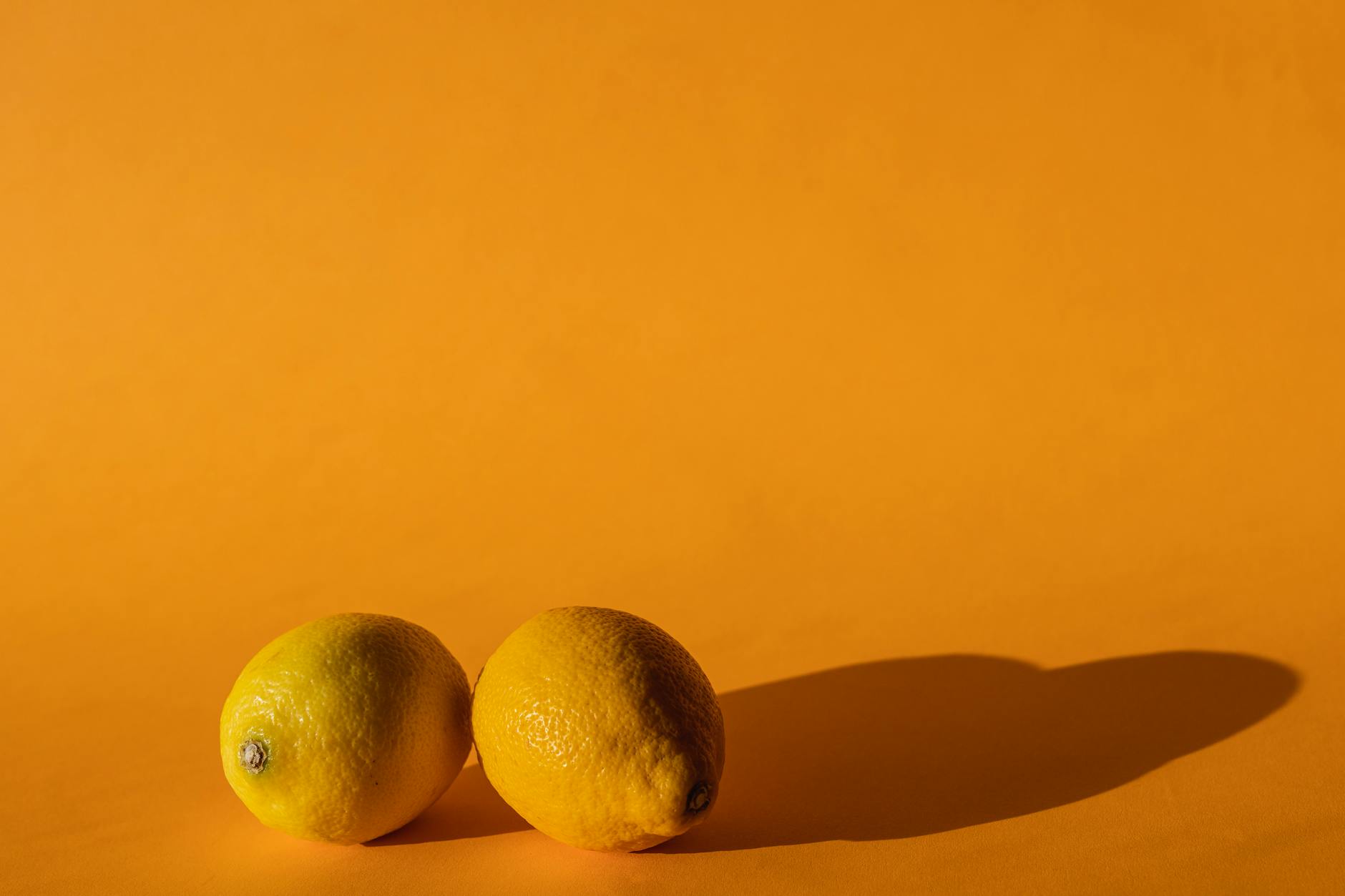 A hand holding a fresh lemon against a soft pink background